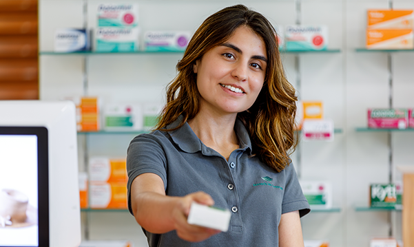 Eine Mitarbeiterin der Pluwig Apotheke steht vor dem Medikamentenregal und hält ein Medikament in der Hand.