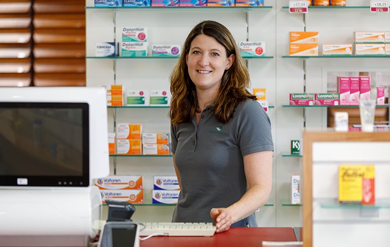 Eine Mitarbeiterin steht hinter dem Tresen am Pc der Pluwig Apotheke.