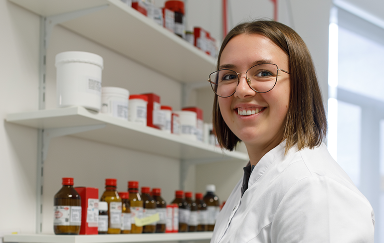 Eine Mitarbeiterin der Pluwig Apotheke steht vor dem Medikamentenregal.