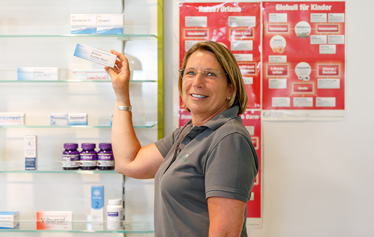 Eine Mitarbeiterin steht von dem Medikamentenregal und hält ein Medikament in der Hand.