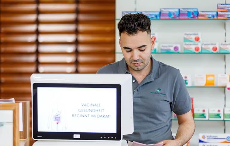 Der Inhaber der Pluwig Apotheke steht vor dem Medikamentenregal und arbeitet am Pc.