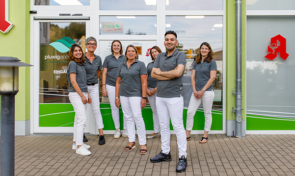 Das Team der Pluwig Apotheke in Pluwig steht vor der Apotheke. Sie tragen grau Shirts mit dem Logo der Apotheke.