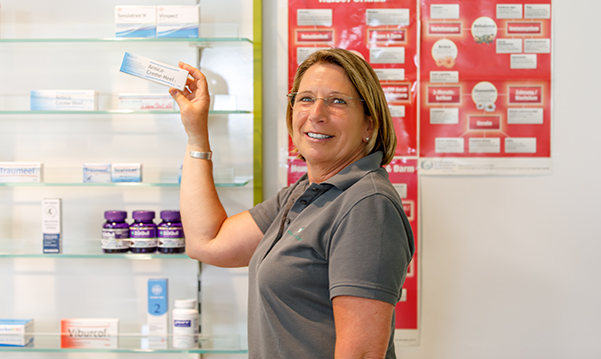 Eine Mitarbeiterin steht von dem Medikamentenregal und hält ein Medikament in der Hand.